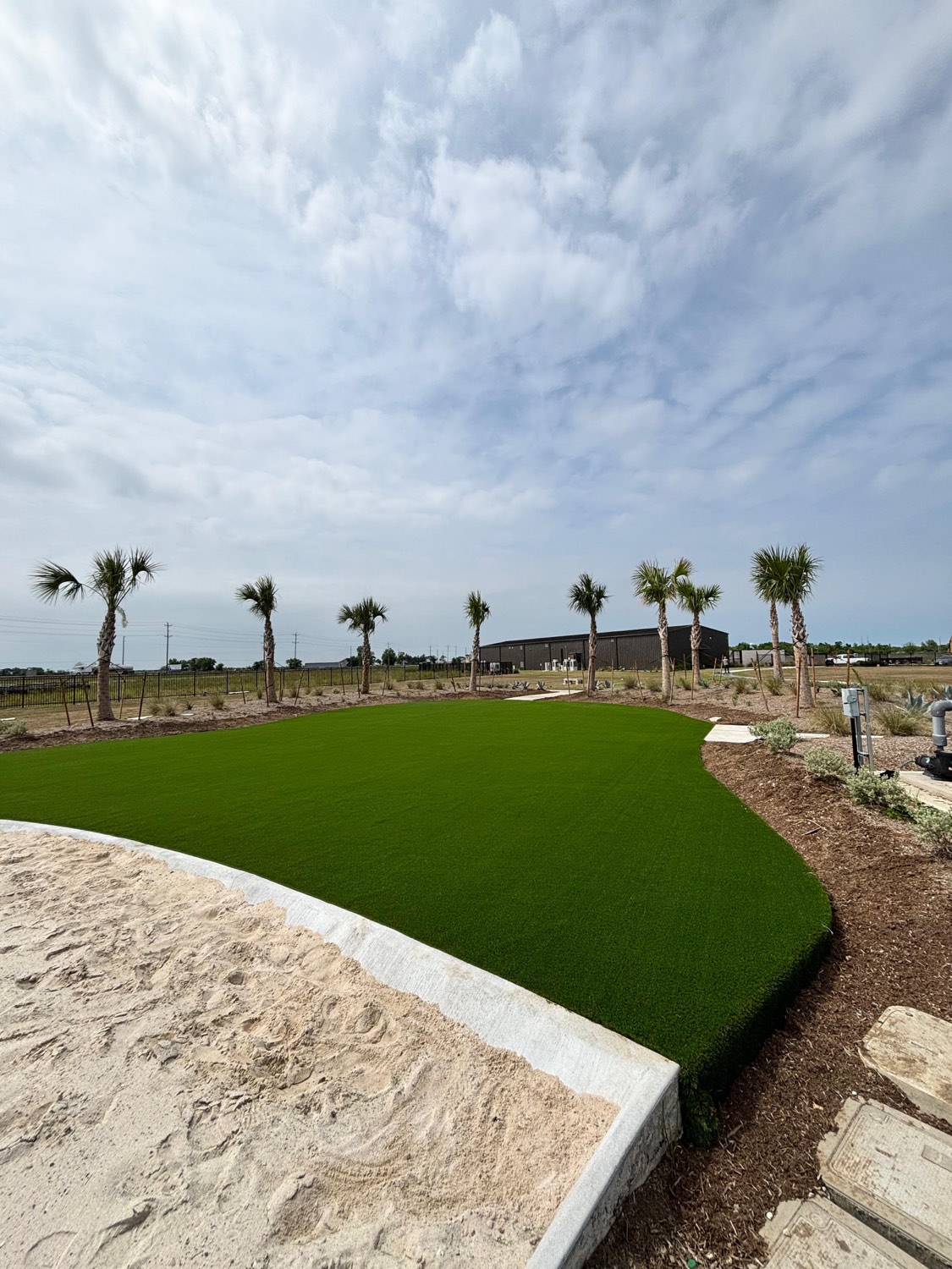 Instalación comercial de grama artificial con palmeras junto a laguna